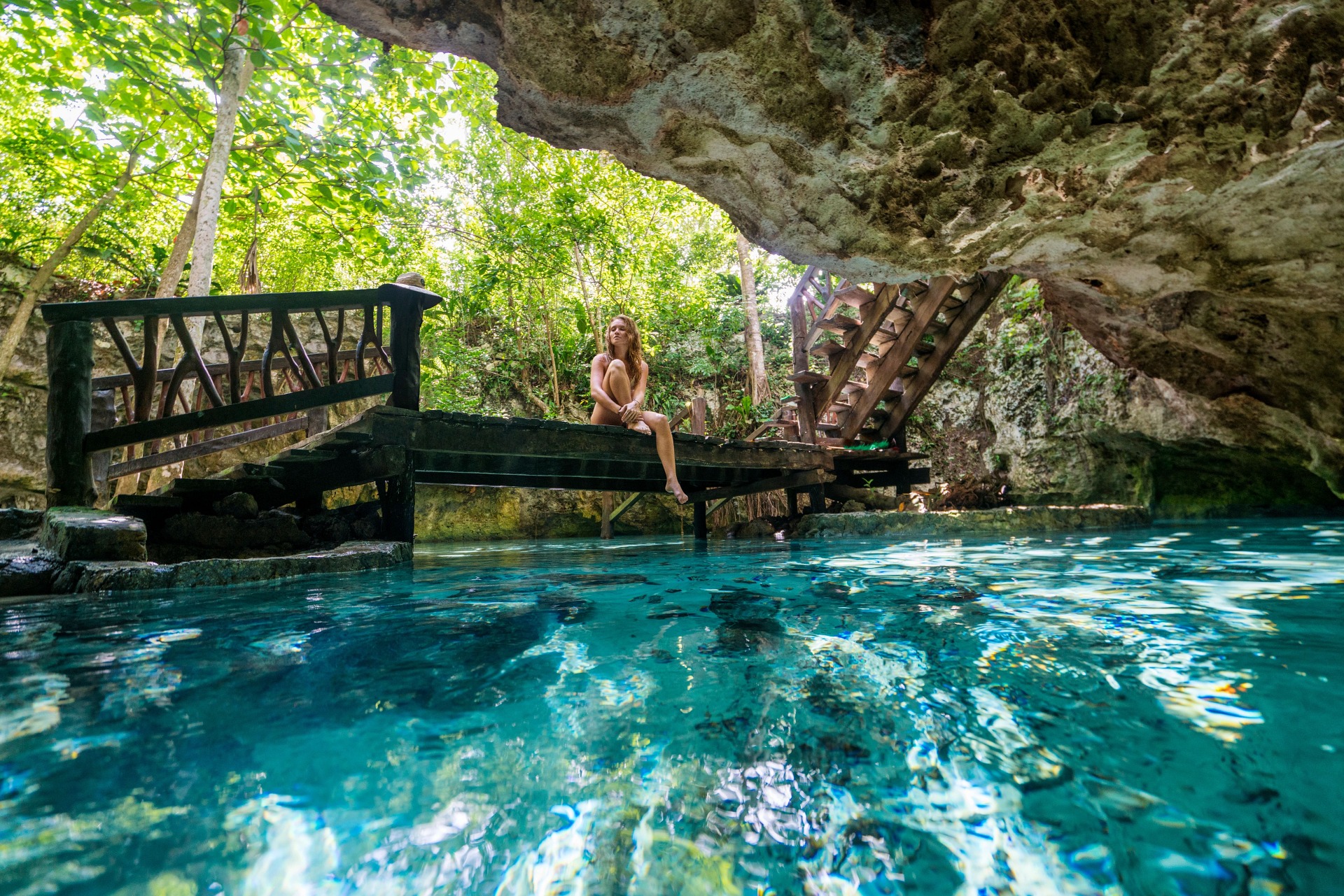 Costa Maya, Mexico, Yucatán, woman sitting on edge of walkway, bridge, over large underground pool, limestone cave, tropical trees in background, fun, adventure, resting, relaxing